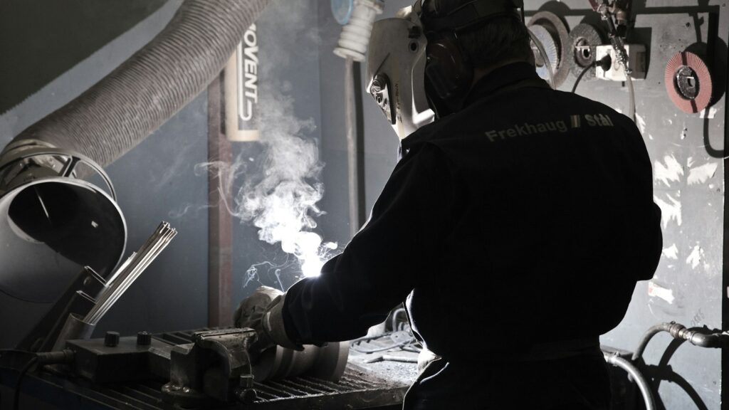 Worker in a protective suit welding metal, representing hands-on repair of worn industrial parts