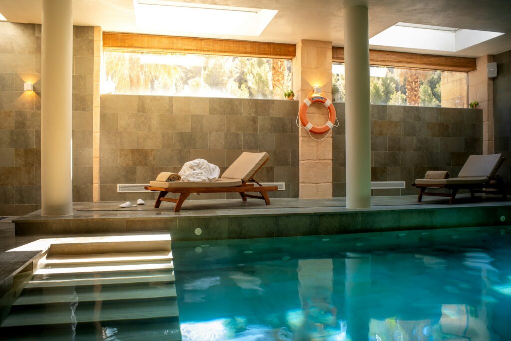 Large swimming pool with a lounge chair beside it in a serene indoor setting with palm tree views